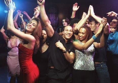 A mixed crowd with their hands up on a dance floor