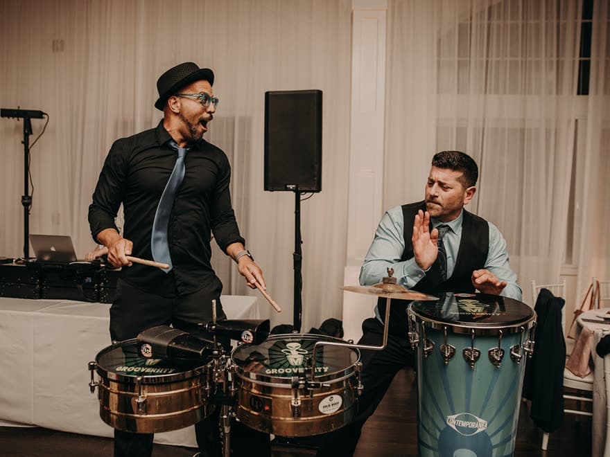 Percussionist mid-jump over timbales beside a drummer