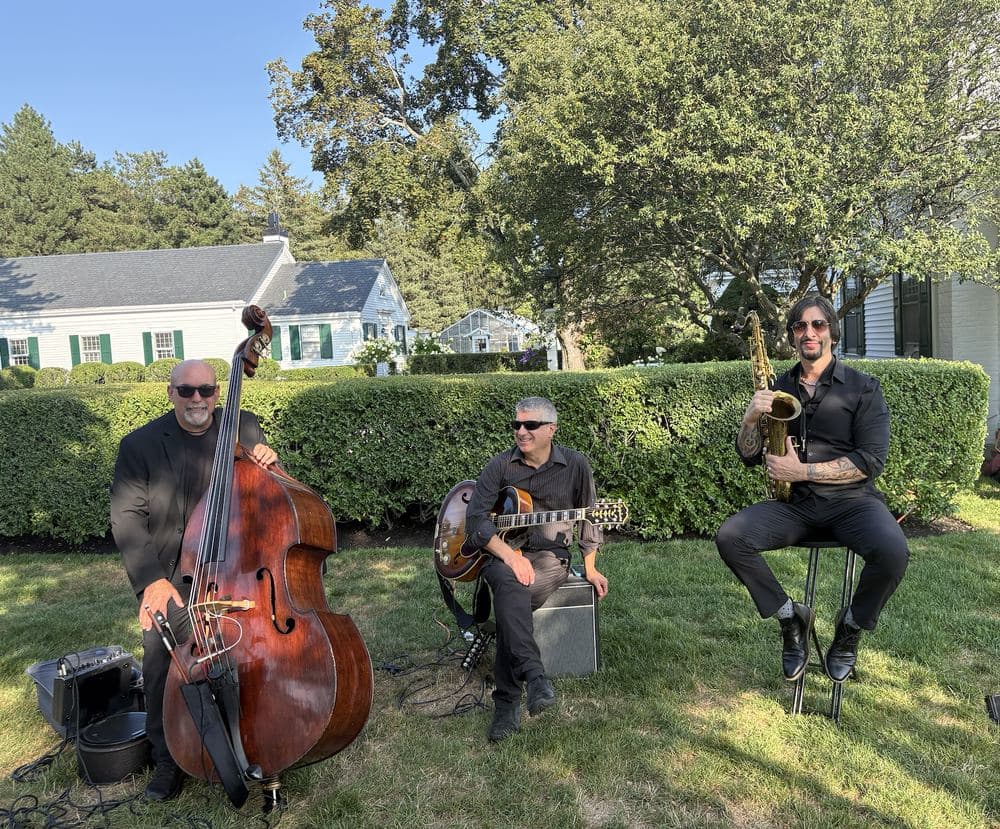 The jazz trio playing on a lawn beside a New England house