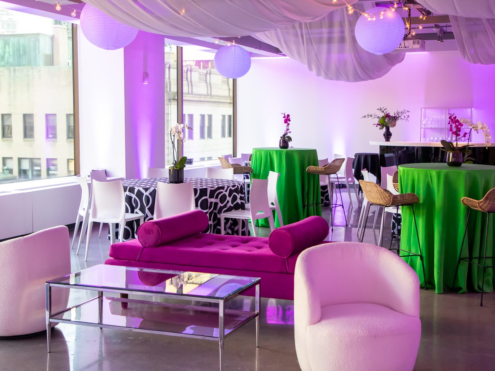 An event space dressed in purple uplighting with draped ceilings and cocktail tables
