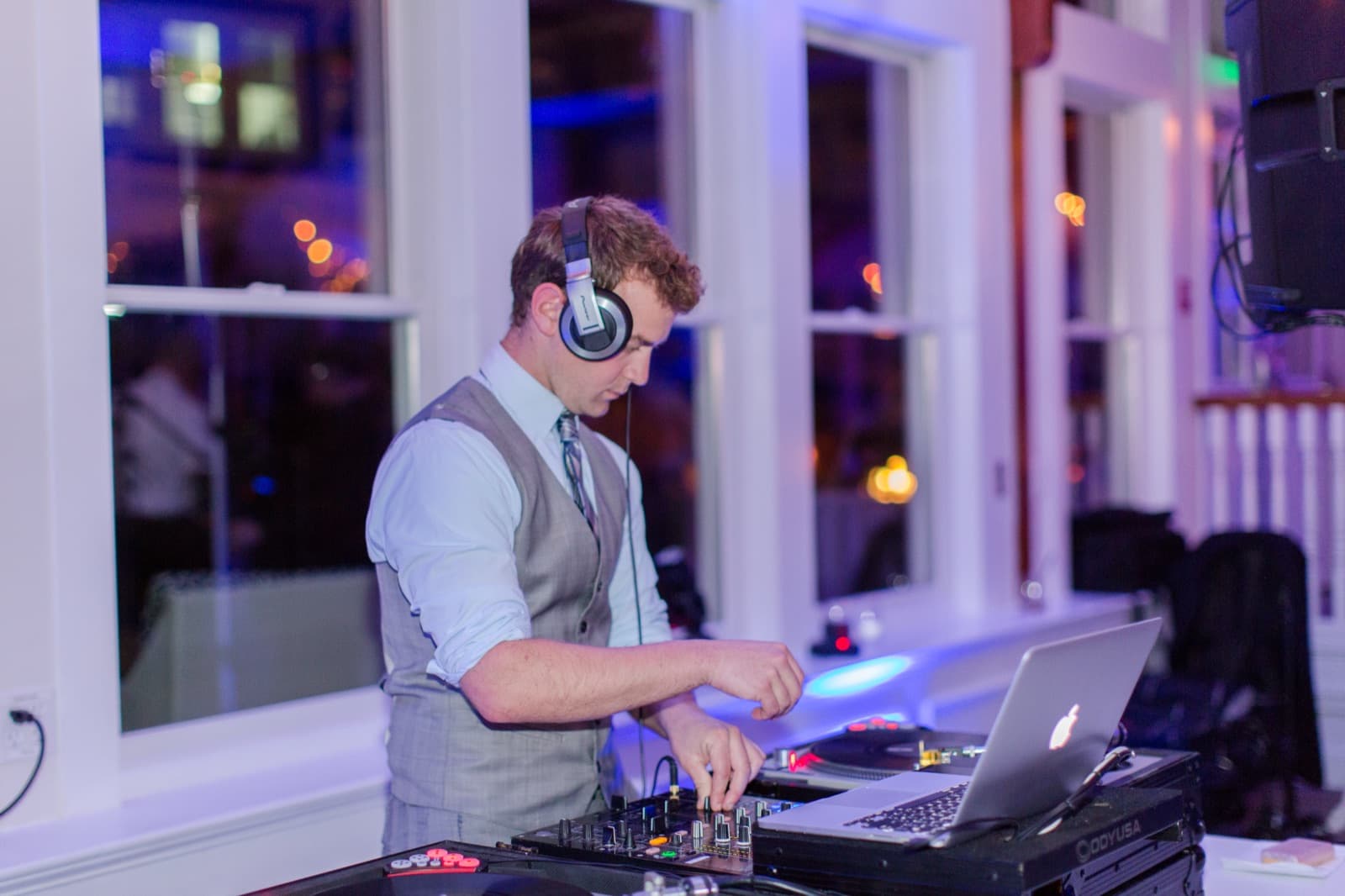 A DJ working the decks in front of harbor windows at dusk