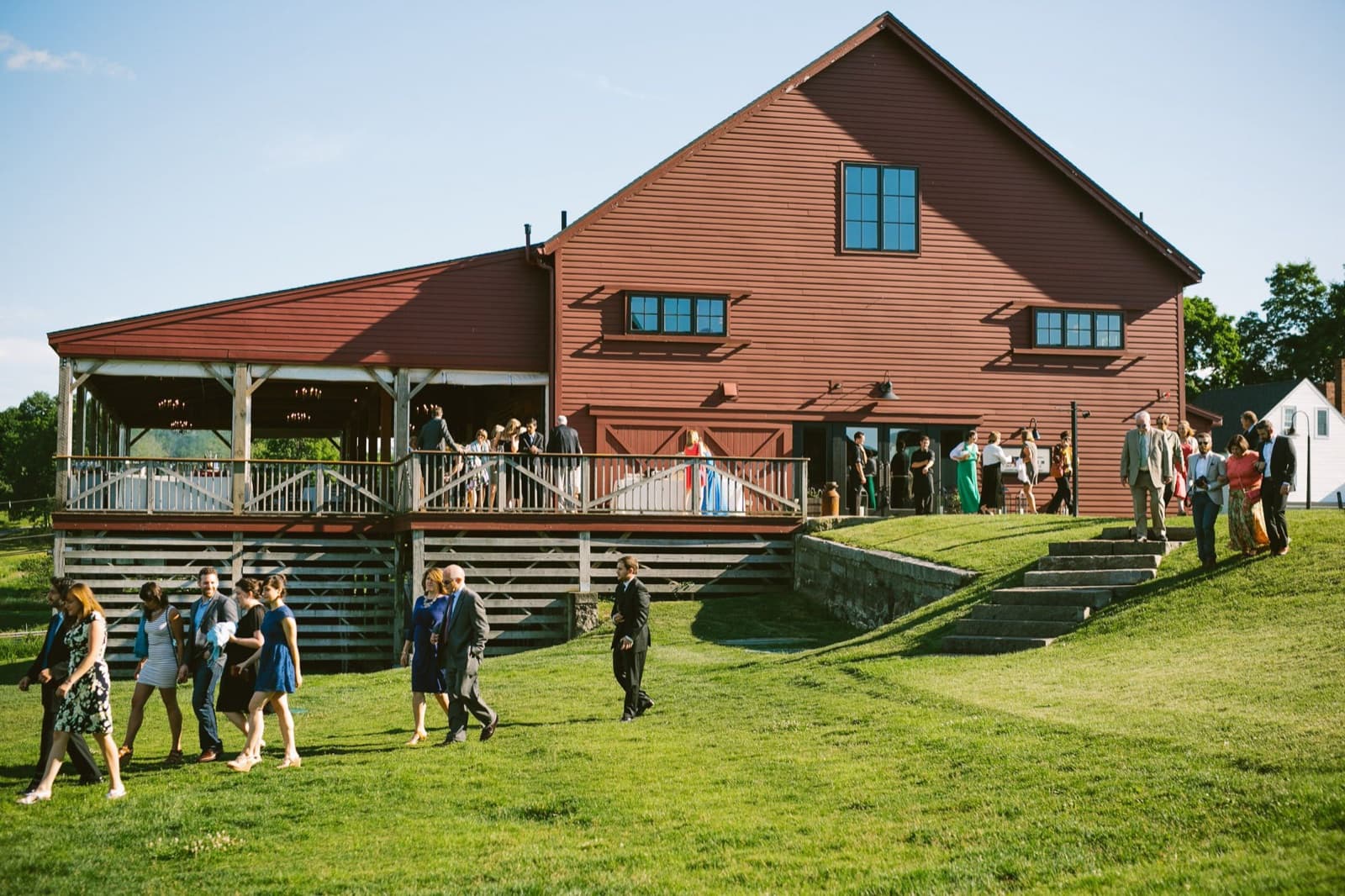 The red Barn at Gibbet Hill with its covered back deck, guests walking up the lawn in evening light