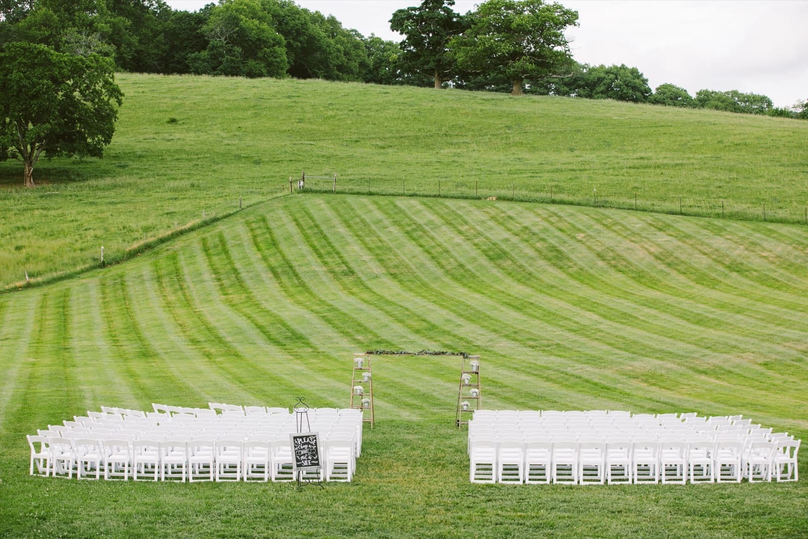White ceremony chairs set on the striped lawn below the rolling hill at The Barn at Gibbet Hill