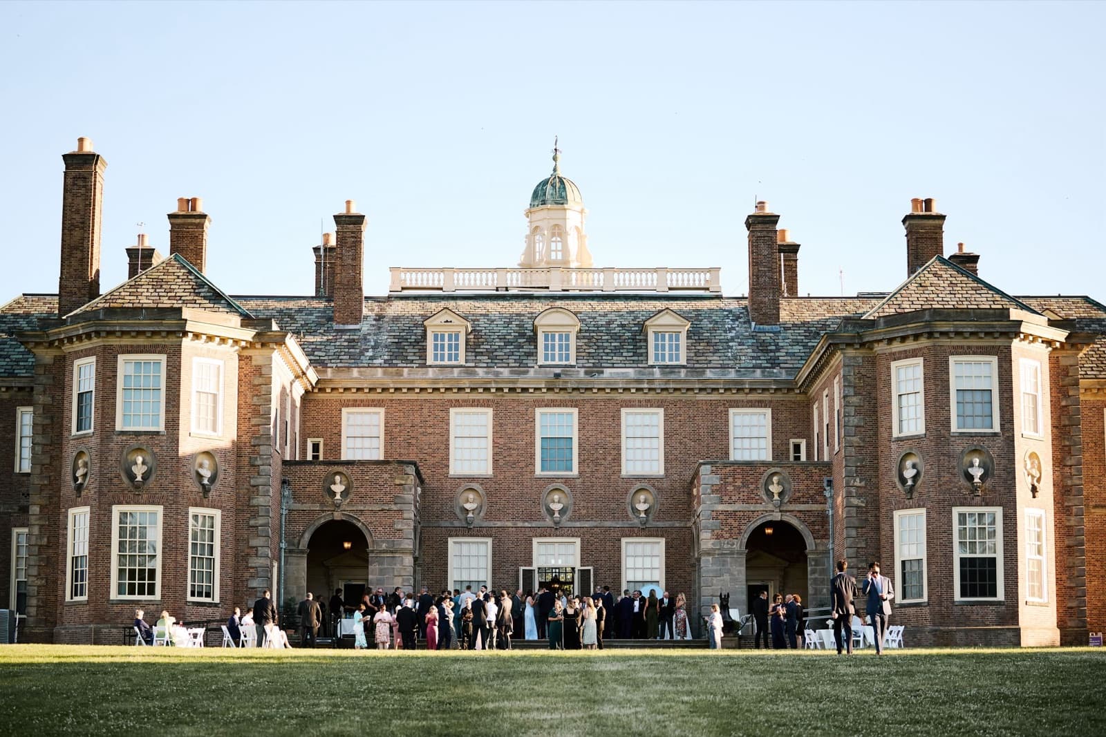 Guests gathered outside the brick Great House at the Crane Estate in evening light