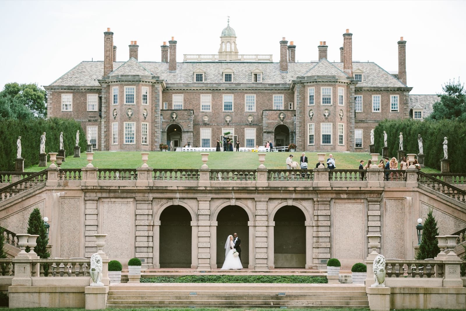 The brick Great House at the Crane Estate above its stone terraces and arches, guests on the lawn at the top