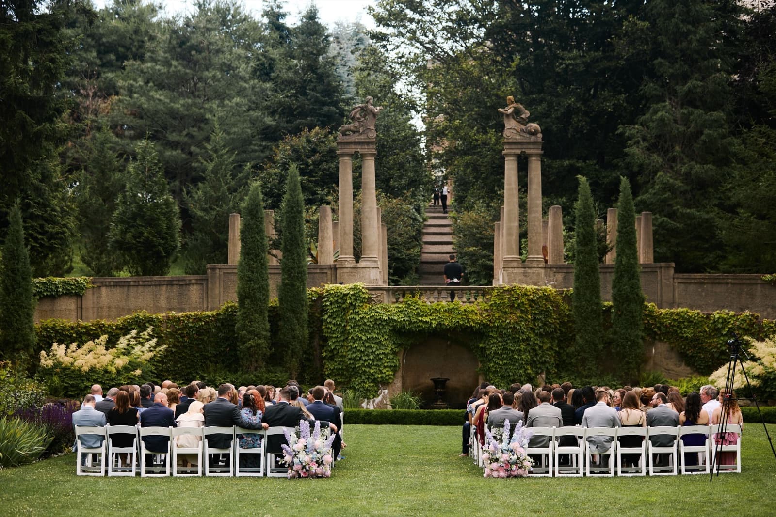 A ceremony in the Italian Garden at the Crane Estate, guests seated before the stone columns and cypress trees