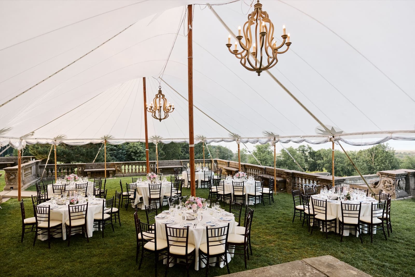 The sailcloth tent at the Crane Estate set for dinner, round tables under chandeliers with the treetops beyond