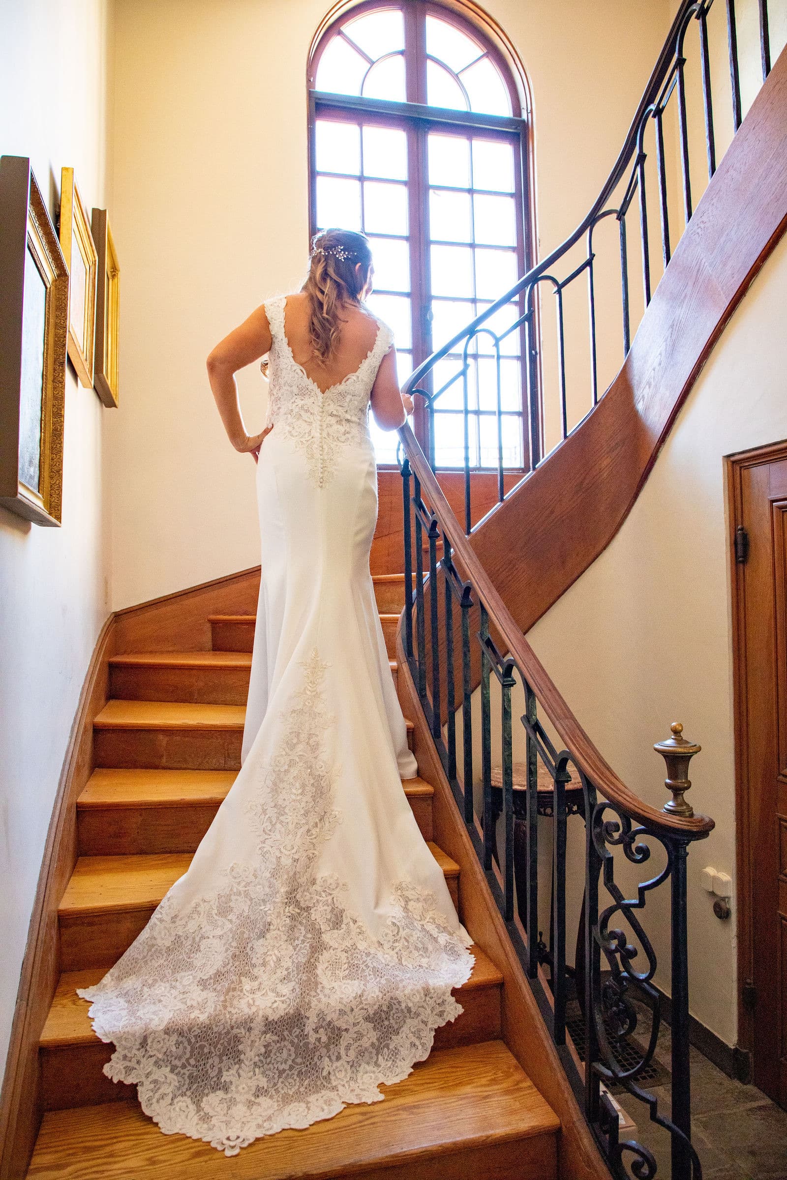 A bride on the winding wooden staircase inside Misselwood, under the arched window