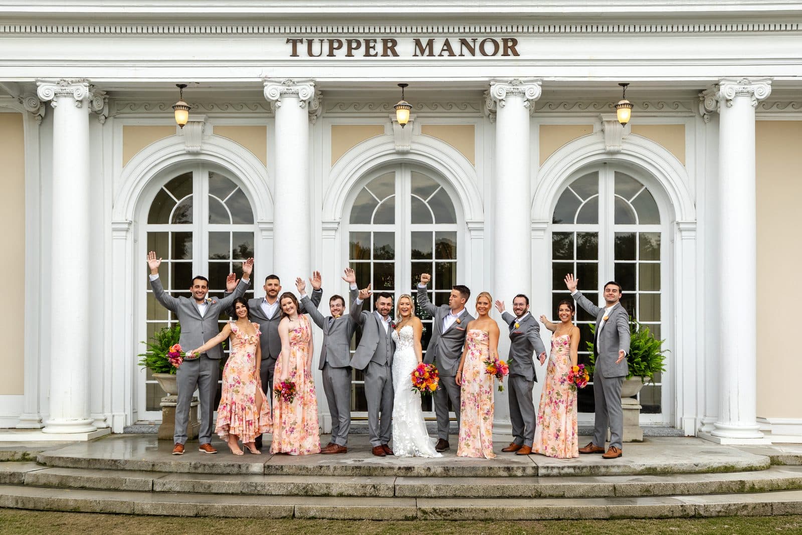 A wedding party cheering on the front steps of Tupper Manor under the columns
