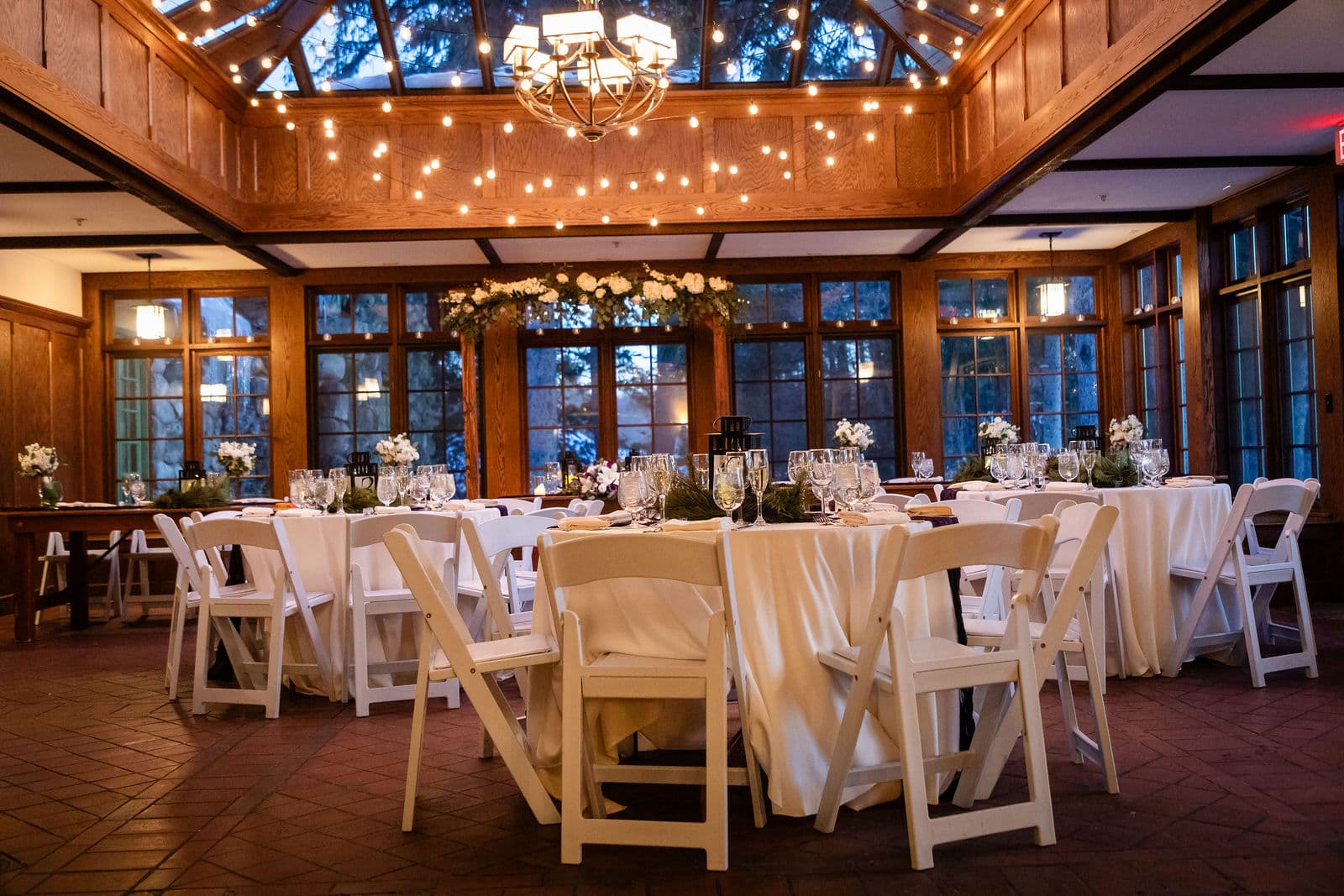 The same conservatory set for dinner with round tables under the string lights