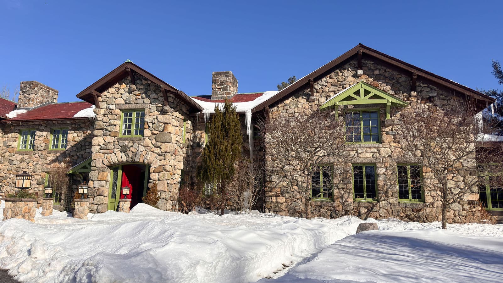 The fieldstone front of the Willowdale Estate mansion with its red door, under a blue winter sky