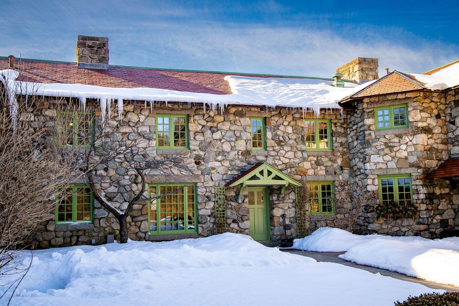 The fieldstone front of the Willowdale Estate mansion in snow, green trim and icicles along the roofline