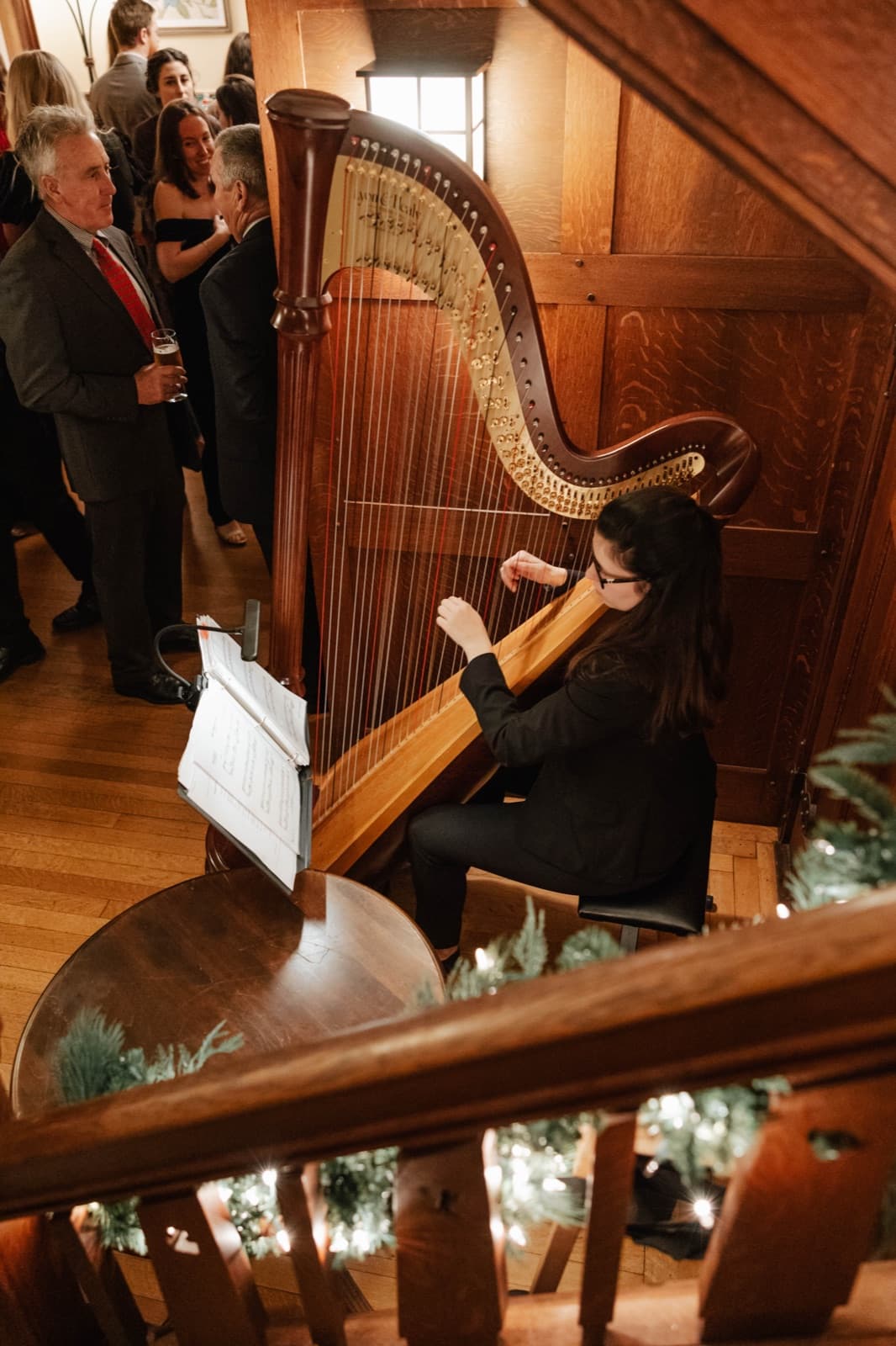 A C-Zone harpist playing beside the carved wooden staircase at Willowdale Estate