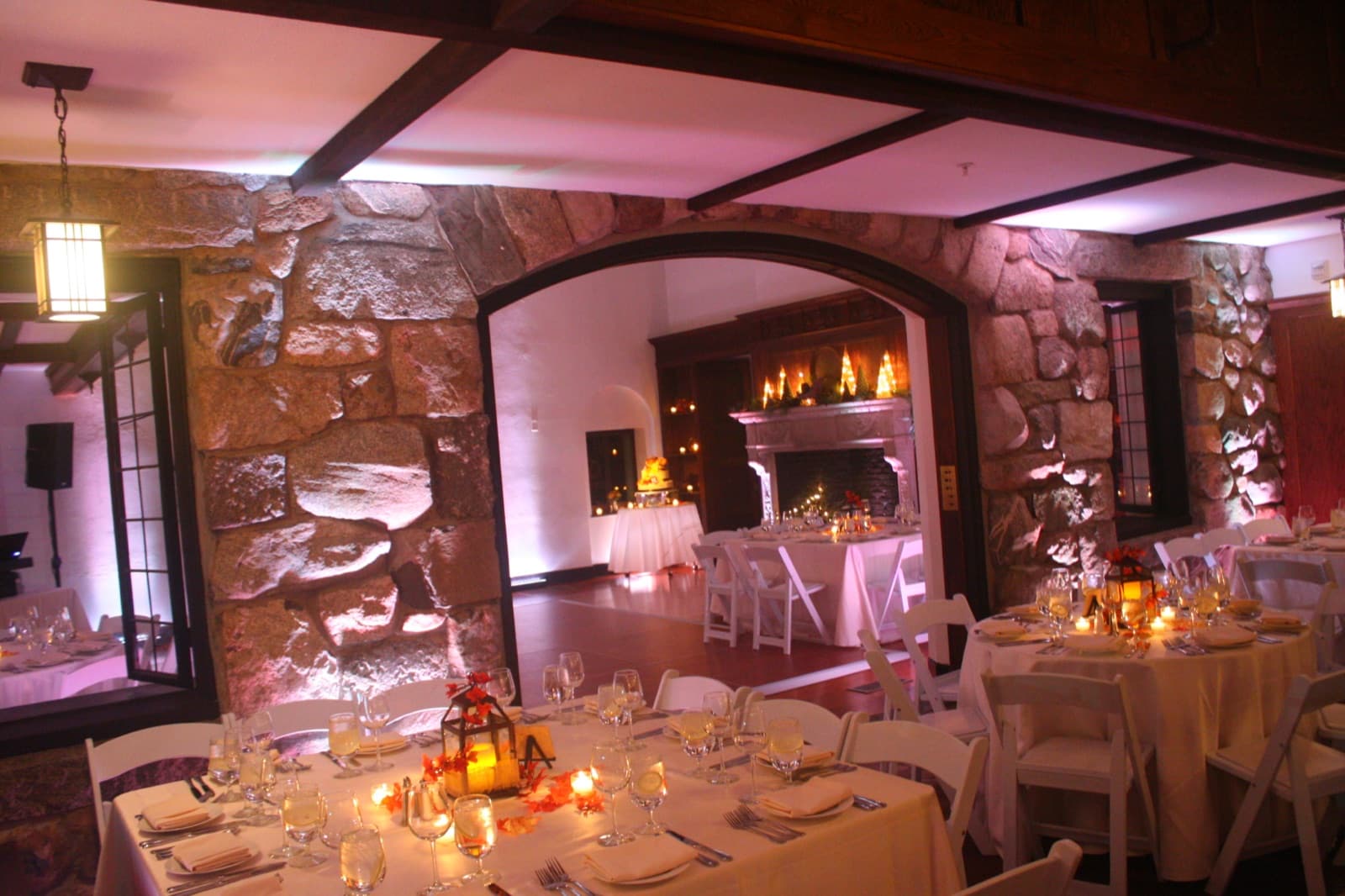 A stone-walled dining room at Willowdale Estate in soft white uplighting, candlelit tables under the arch