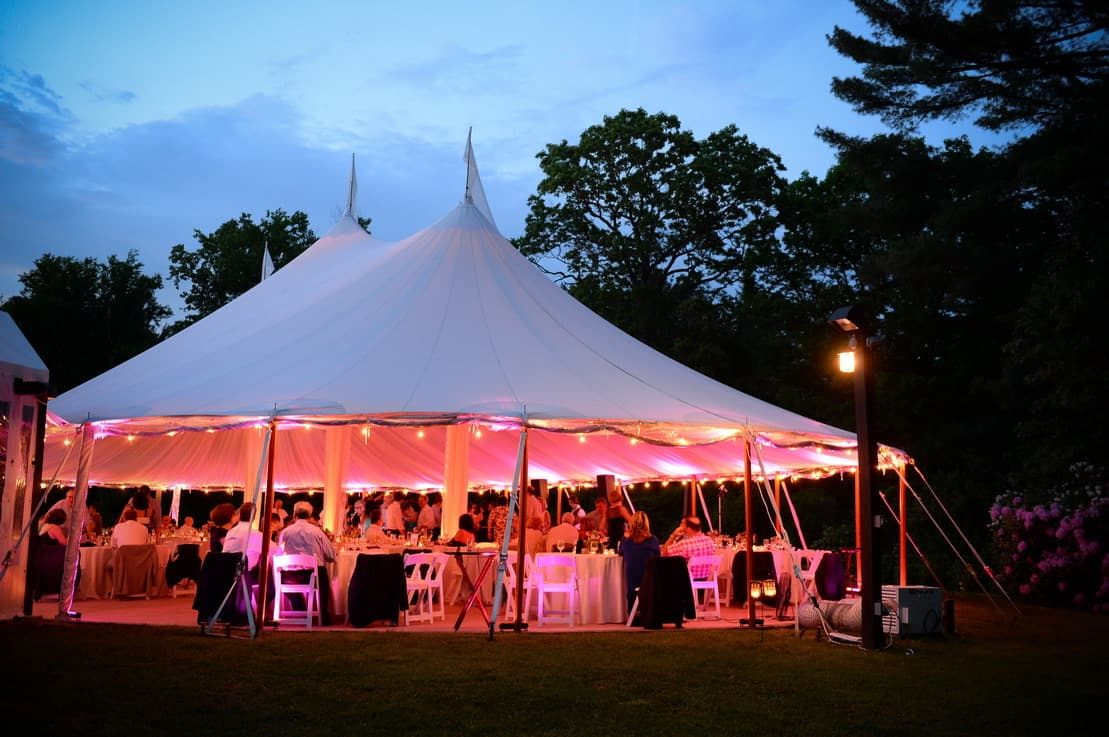 The Willowdale Estate Sperry tent at dusk, its peaks against the sky and the inside glowing over the dinner tables