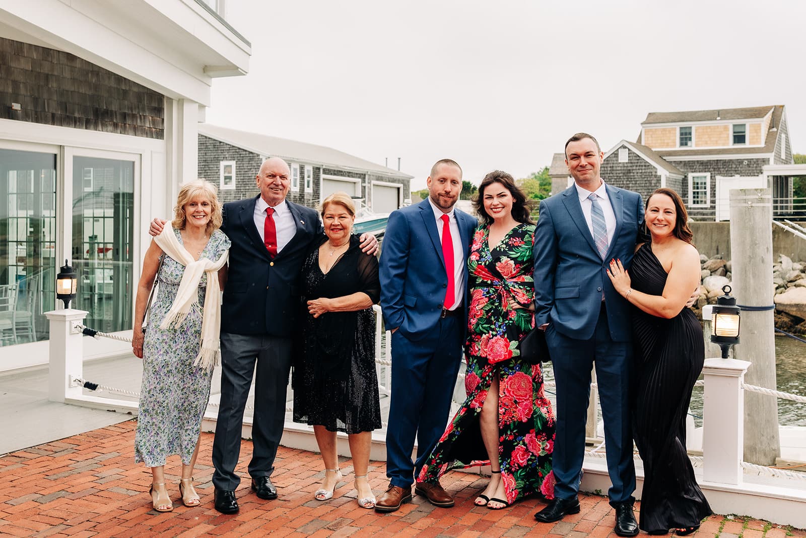 Wedding guests on the brick patio outside the Harbor Room at Wychmere, the harbor and shingled buildings behind them