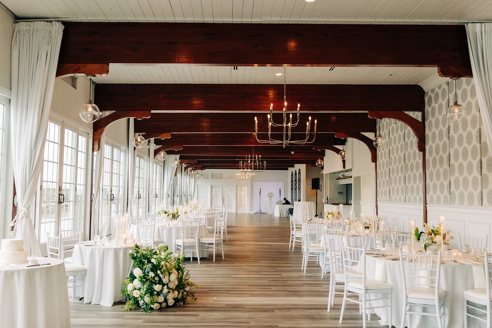 The length of the Harbor Room at Wychmere Beach Club, dark wood beams and chandeliers over round tables running to the far end