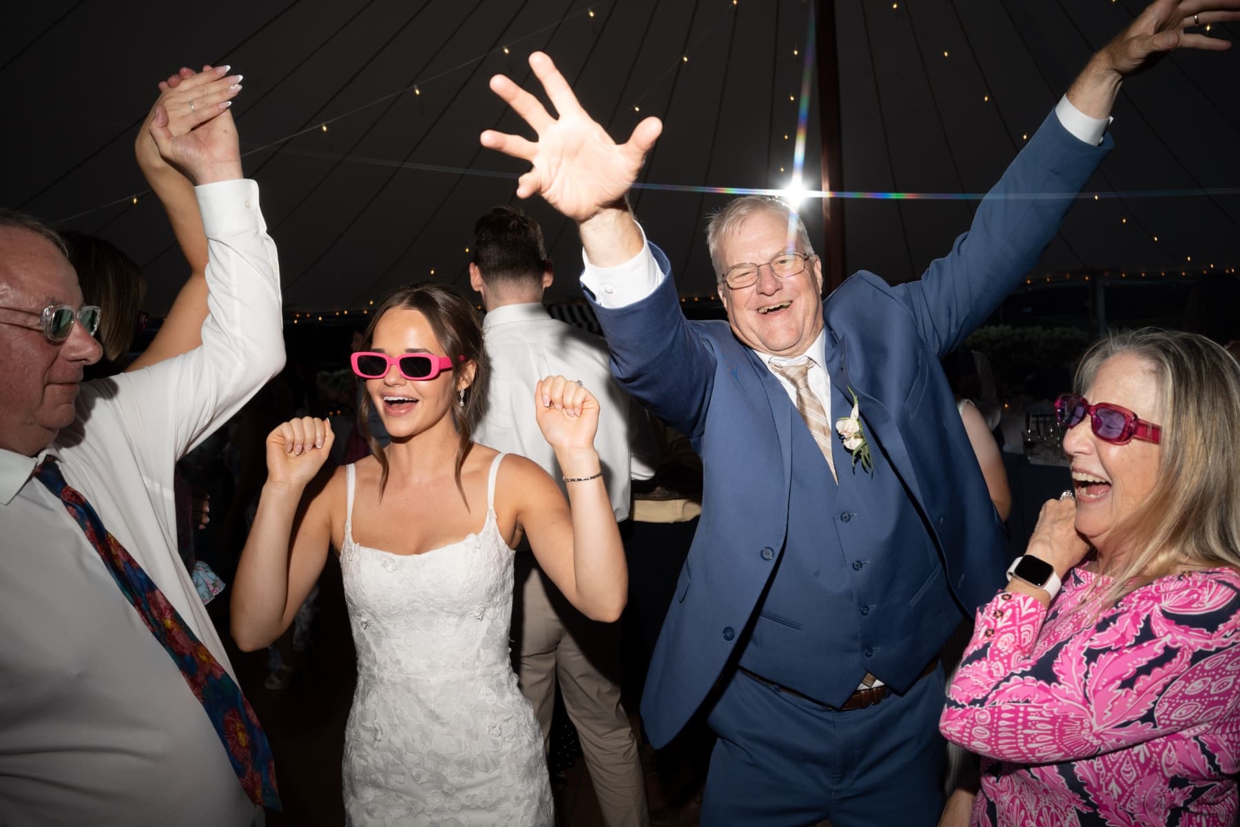 Bride in pink sunglasses dancing with her parents' generation under a sailcloth tent