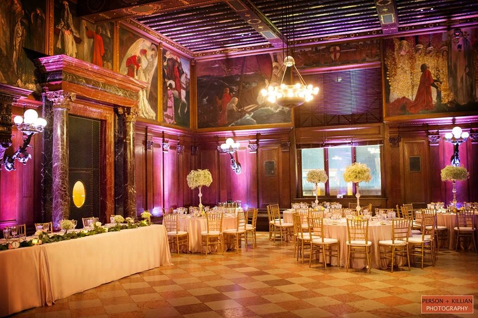 The Boston Public Library's Abbey Room in magenta uplighting, dressed for a seated dinner beneath its murals