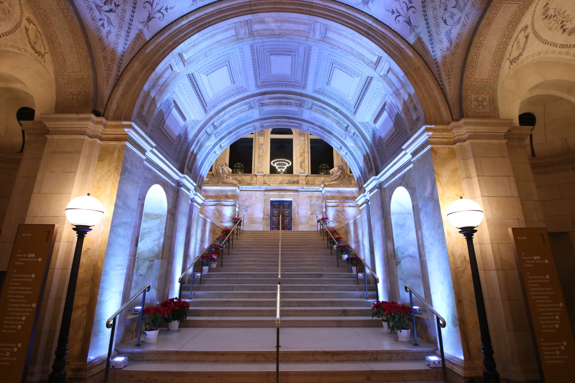 The Boston Public Library's McKim entrance staircase in lavender uplighting, with the stone lions on the landing