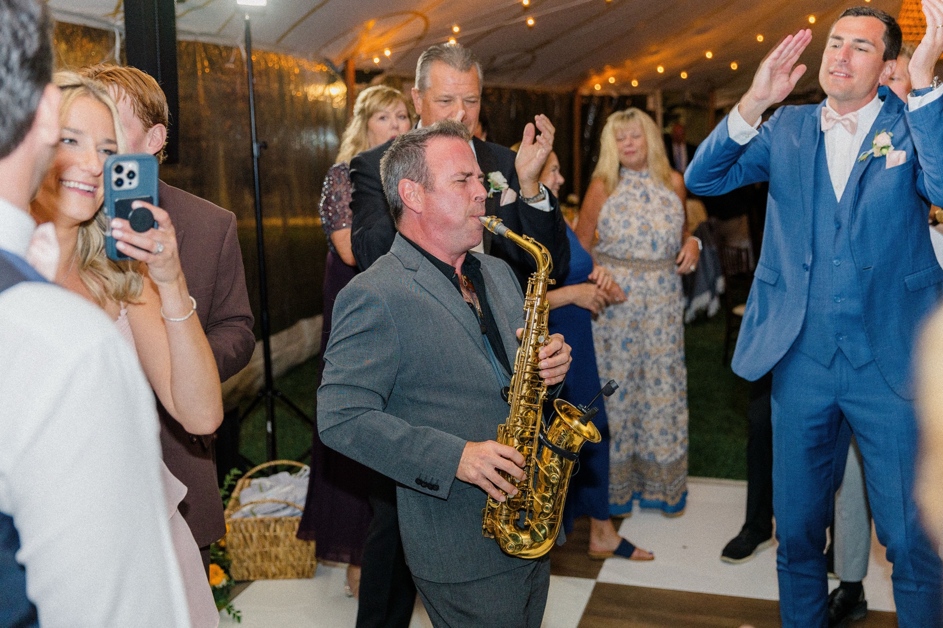 A saxophonist playing on a tented dance floor while guests clap around him